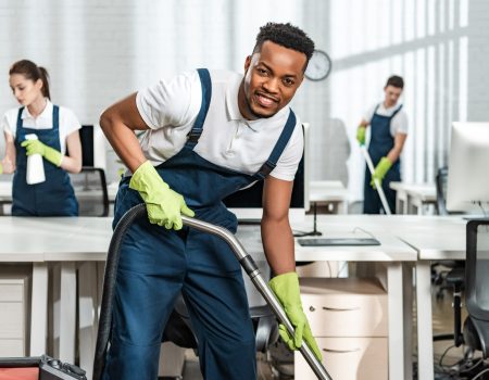 cheerful african american cleaner vacuuming floor while looking cheerful african american cleaner vacuuming floor while looking at camera